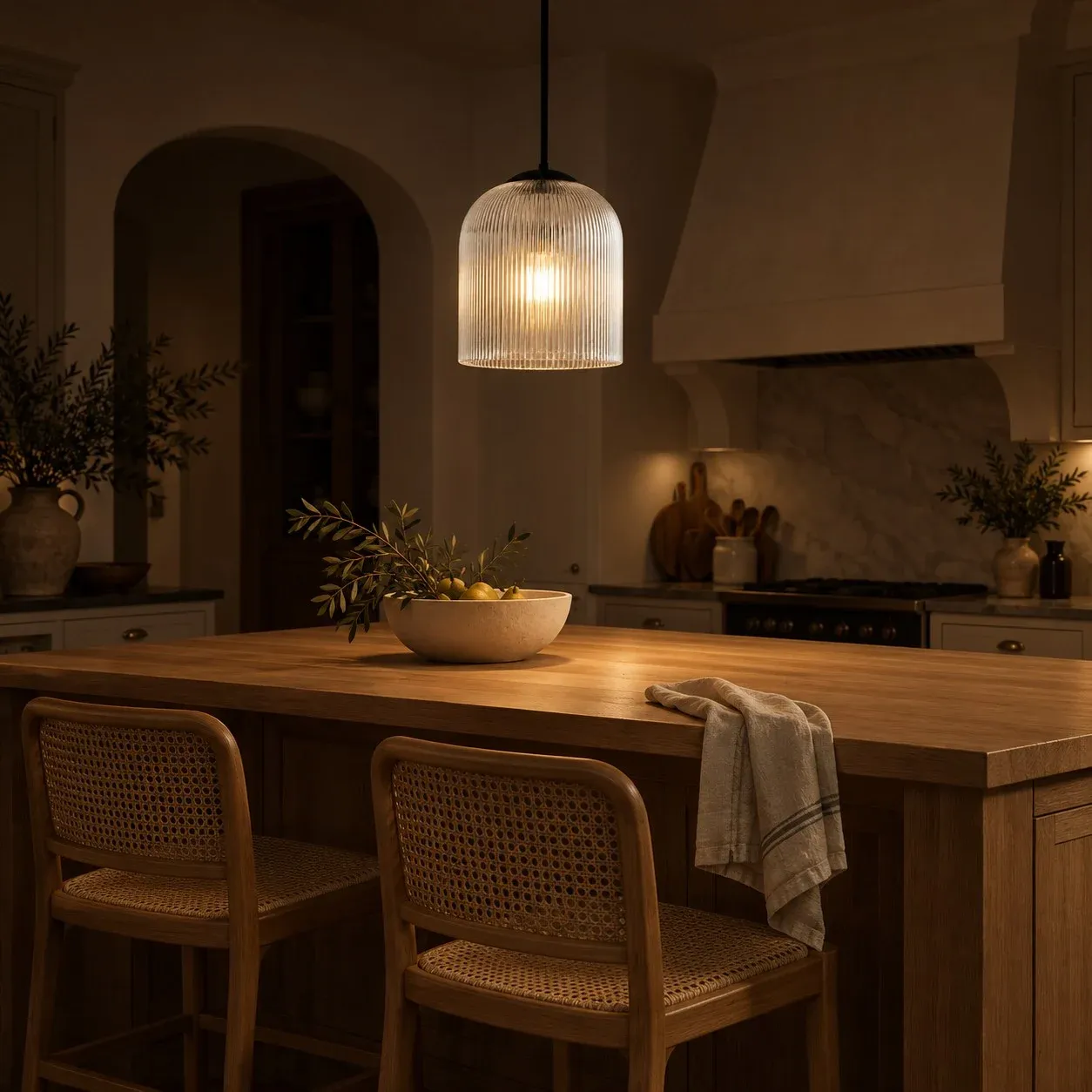 Black ribbed glass bell pendant lit over a kitchen island at night