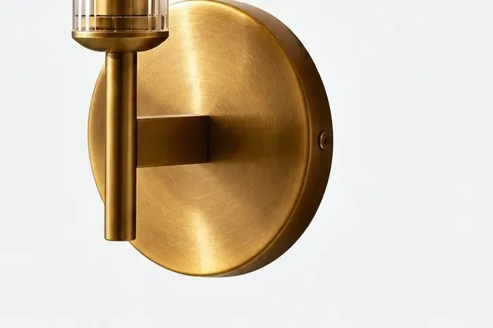 Brushed brass round backplate, short arm, set screw, and the base of a ribbed glass tube