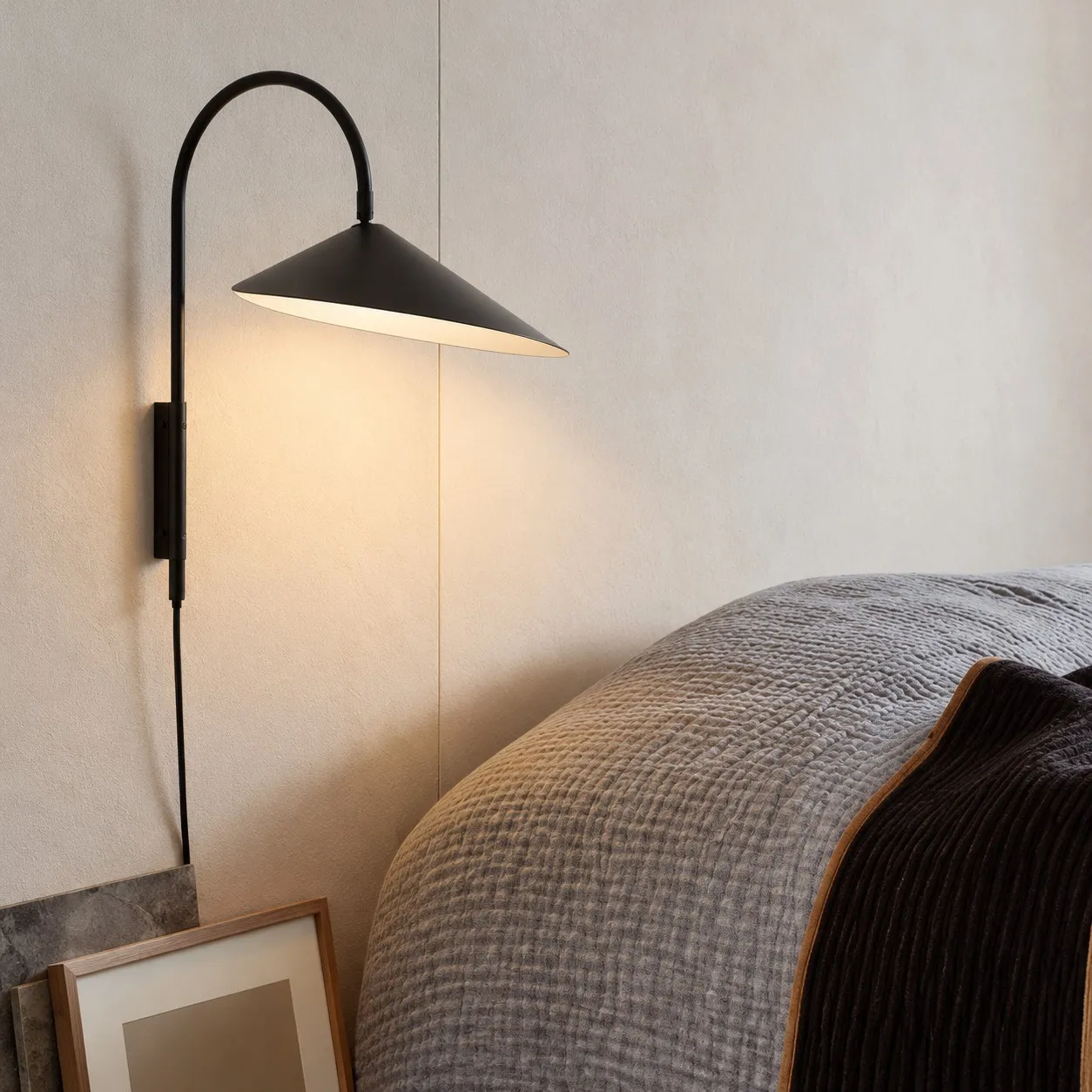 Black swivel wall lamp beside a bed