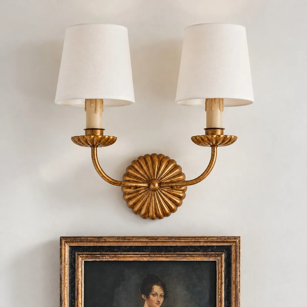 Antique gold double wall lamp above a framed portrait