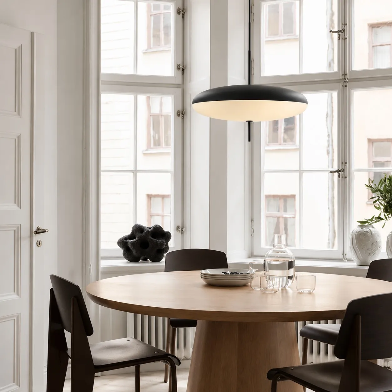Black elliptical pendant above a round table by tall windows